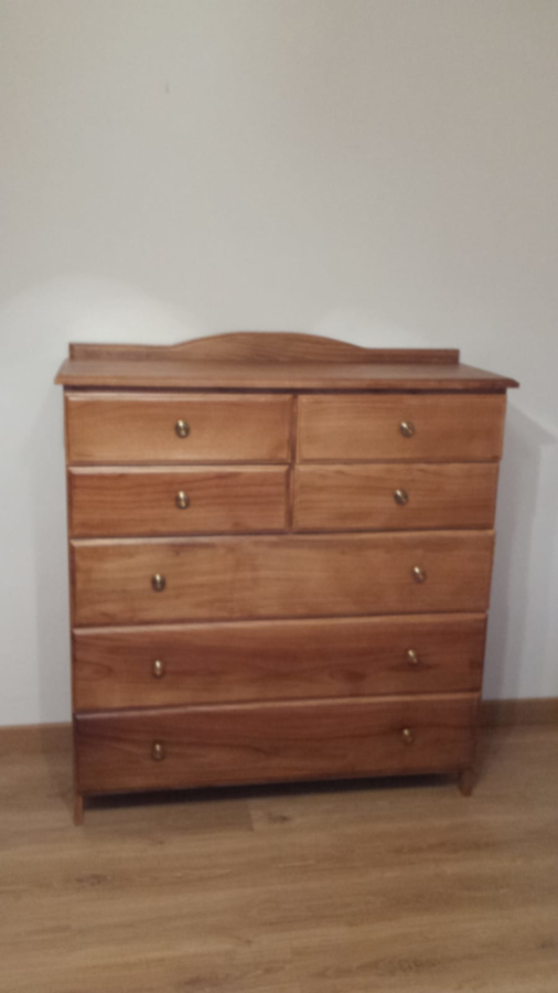 Cómoda de madera con seis cajones, tapa curva y tiradores de latón sobre suelo de madera.