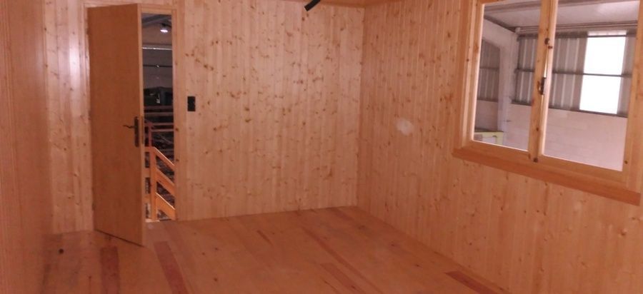 Habitación con paneles de madera, puerta abierta al pasillo y ventana. Suelos y paredes de madera natural.