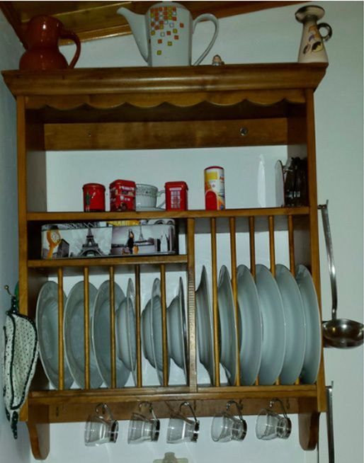 Estante de madera para platos con platos y utensilios de cocina expuestos contra una pared blanca.