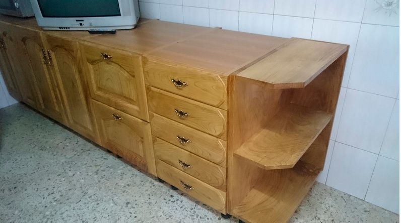 Muebles de cocina de madera con cajones y estantes. Un televisor encima.