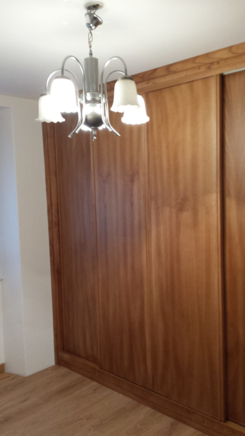 Dormitorio con armario de madera y lámpara de araña plateada con pantallas blancas.