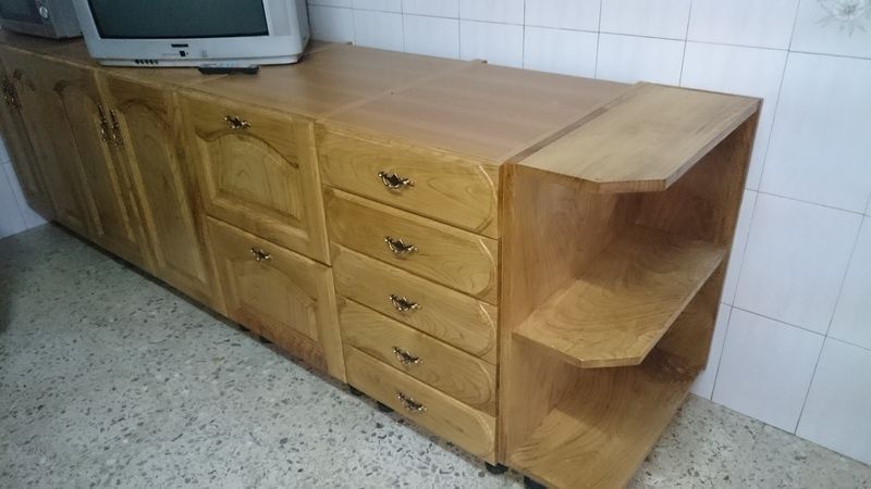 Mueble de madera con cajones y estantes, rematado con un televisor antiguo, apoyado contra una pared de azulejos.