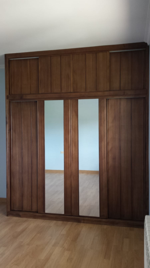 Armario de madera con dos puertas de espejo, apoyado sobre una pared de color azul claro y suelo de madera.