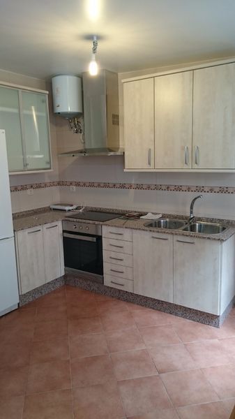 Cocina con gabinetes de madera clara, electrodomésticos de acero inoxidable y pisos de terracota.