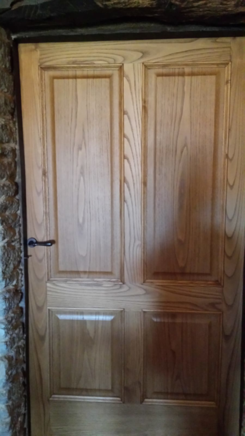 Puerta de madera con paneles y herrajes oscuros colocados en un marco de piedra.