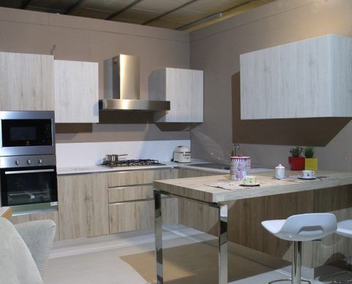 Cocina moderna con gabinetes de madera clara, electrodomésticos de acero inoxidable y barra de desayuno.