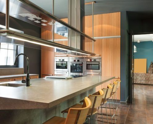 Cocina moderna con electrodomésticos de acero inoxidable, asientos en isla, paneles de madera y paredes oscuras.