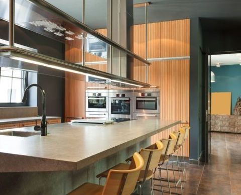 Cocina moderna con electrodomésticos de acero inoxidable, asientos en isla, paneles de madera y paredes oscuras.