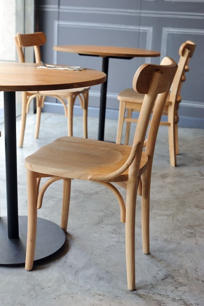 Sillas y mesas de madera en cafetería, tonos neutros, diseño moderno, iluminación suave.