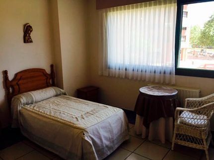 Un dormitorio con una cama, silla, mesa y ventana.