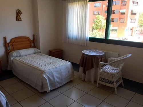 Un dormitorio con una cama, silla, mesa y ventana.