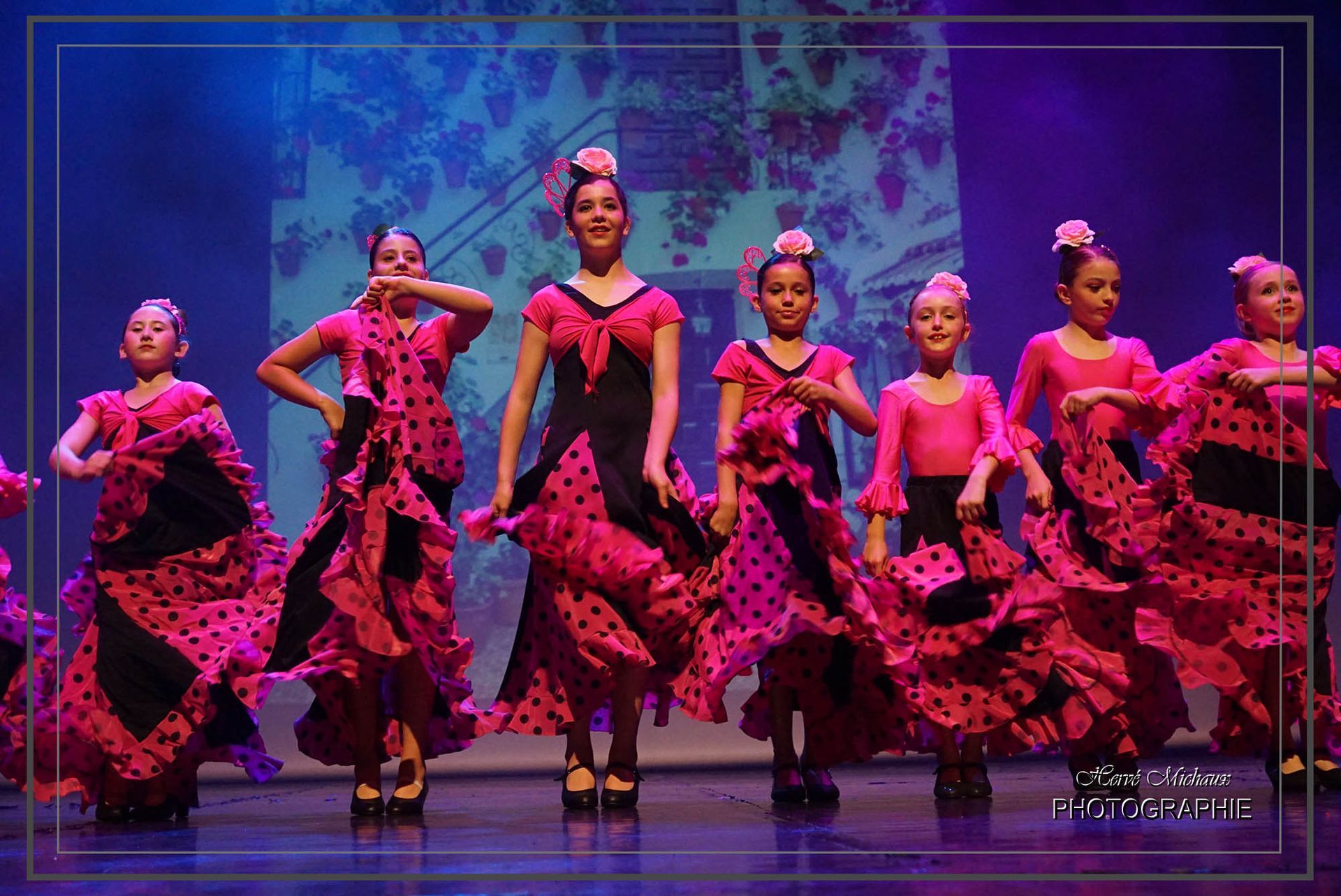 Jeunes danseurs en robes de flamenco roses et noires, se produisant sur scène.