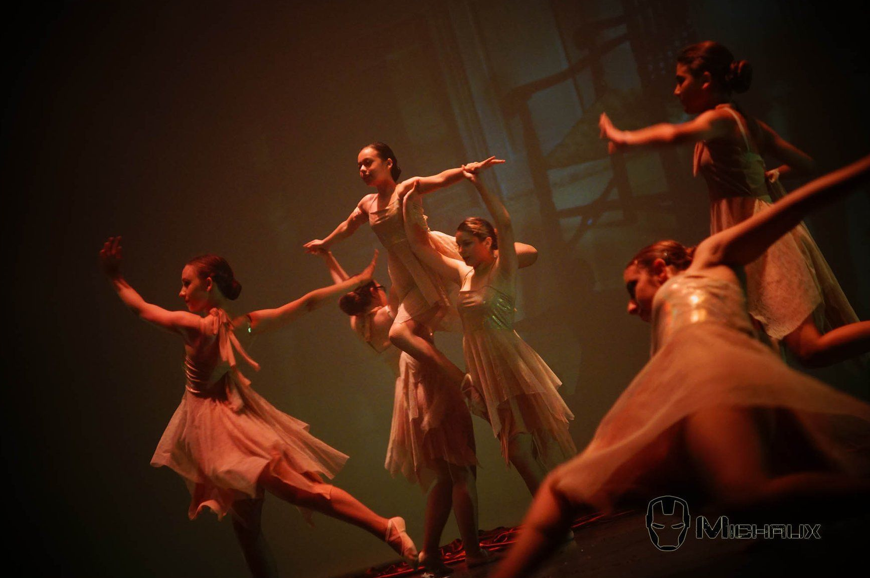 Des danseurs de ballet vêtus de robes blanches fluides se produisent sur scène, les bras tendus.