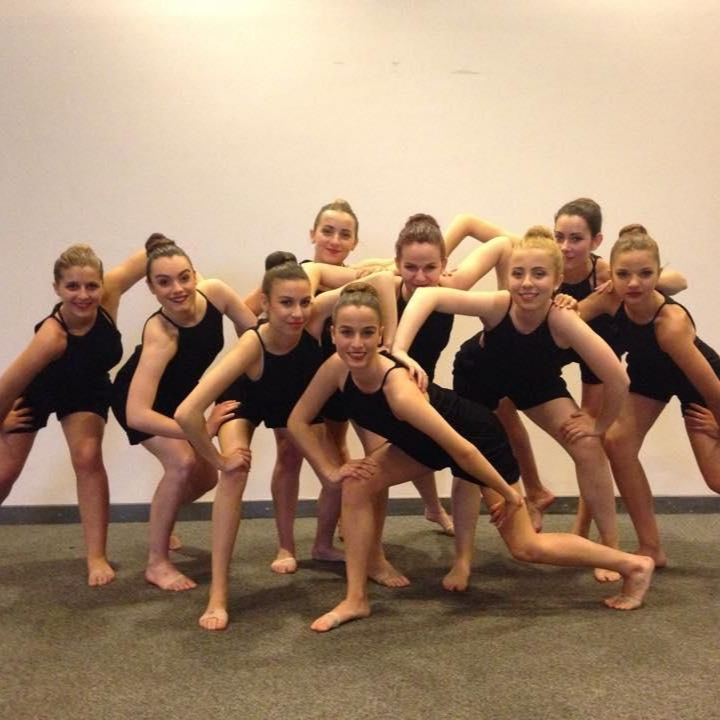Un groupe de danseurs en tenue noire prend des poses spectaculaires. Mur blanc en arrière-plan.