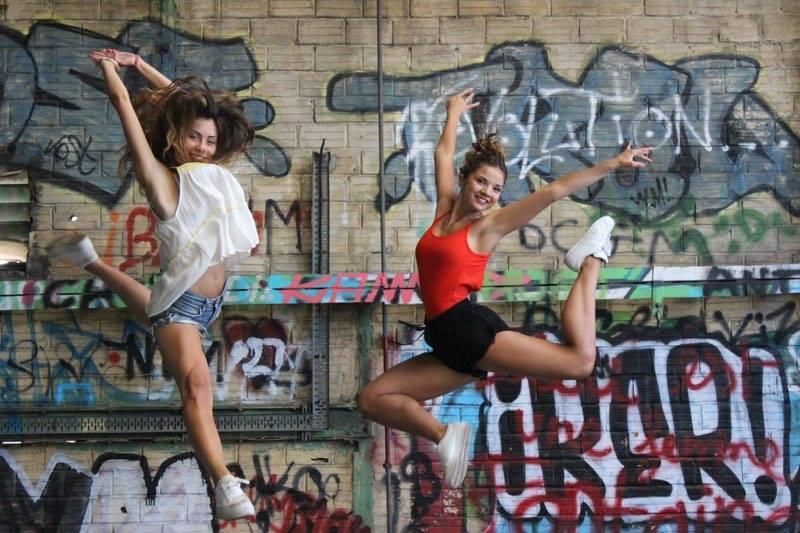 Deux jeunes femmes sautant en l'air, souriantes, devant un mur couvert de graffitis.