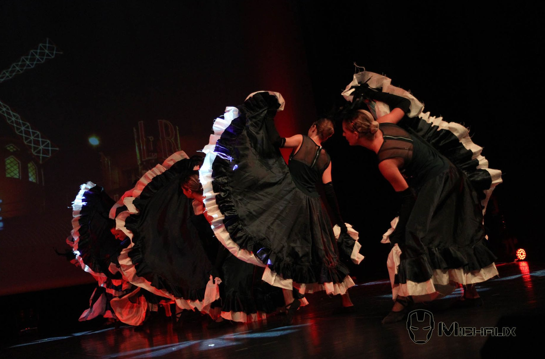 Danseuses en robes de flamenco noires à volants blancs, se produisant sur une scène sombre.