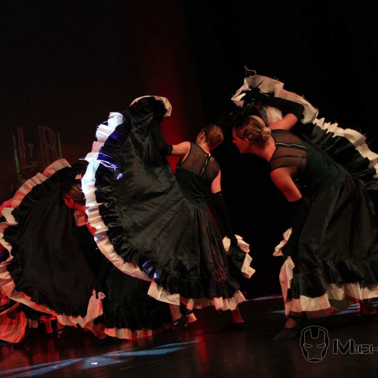 Des danseurs en robes noires avec des bordures blanches se produisent sur une scène.
