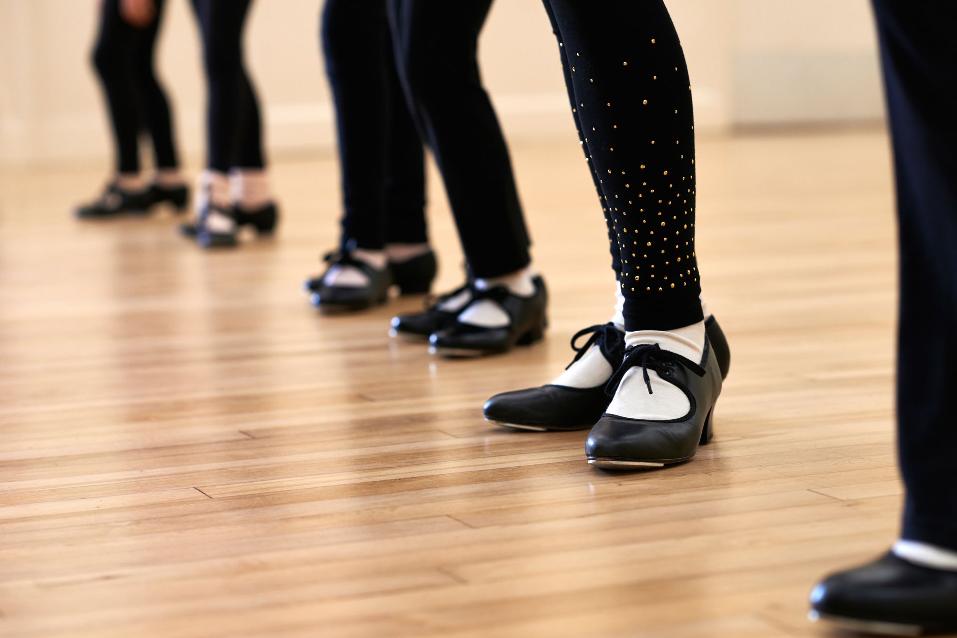 Danseurs de claquettes en leggings noirs et chaussures de claquettes sur un plancher en bois, jambes alignées.