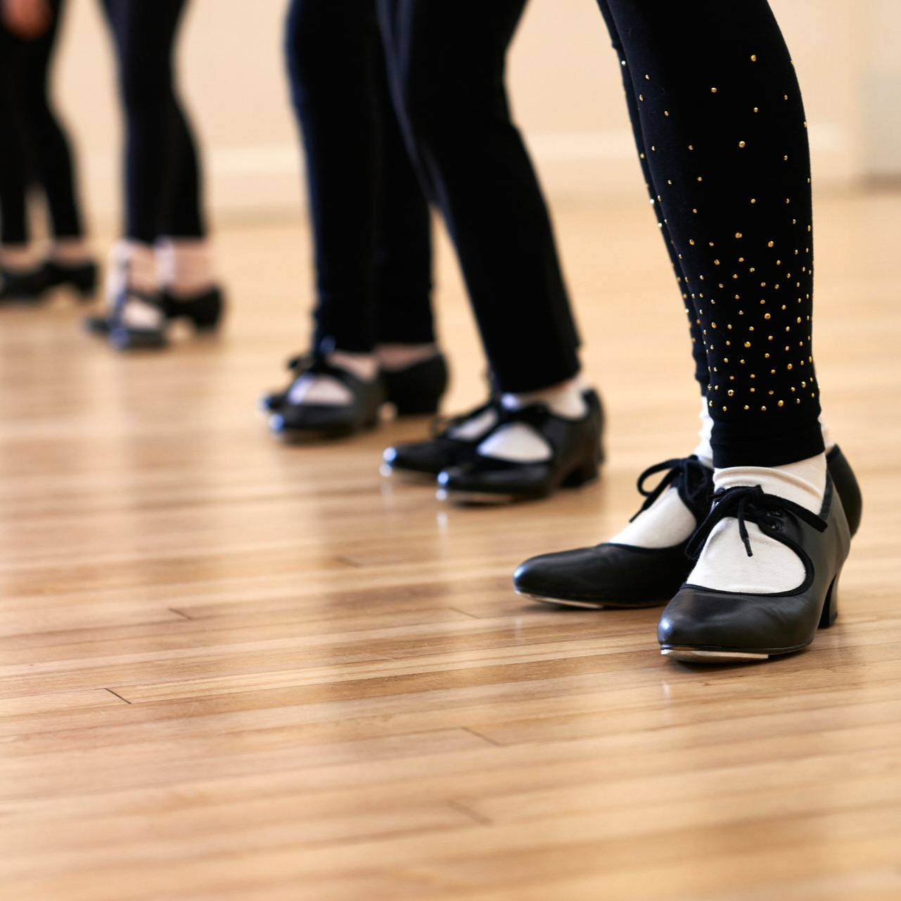 Des danseurs en chaussures de claquettes noires et leggings sur un plancher en bois, s'entraînant.