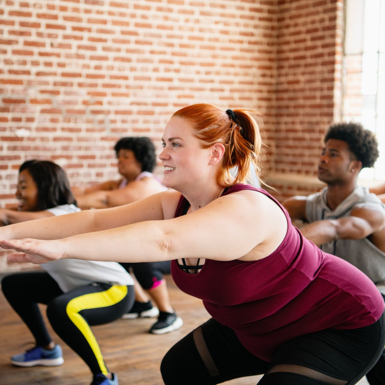 Des personnes dans un cours de fitness font des squats devant un mur de briques.