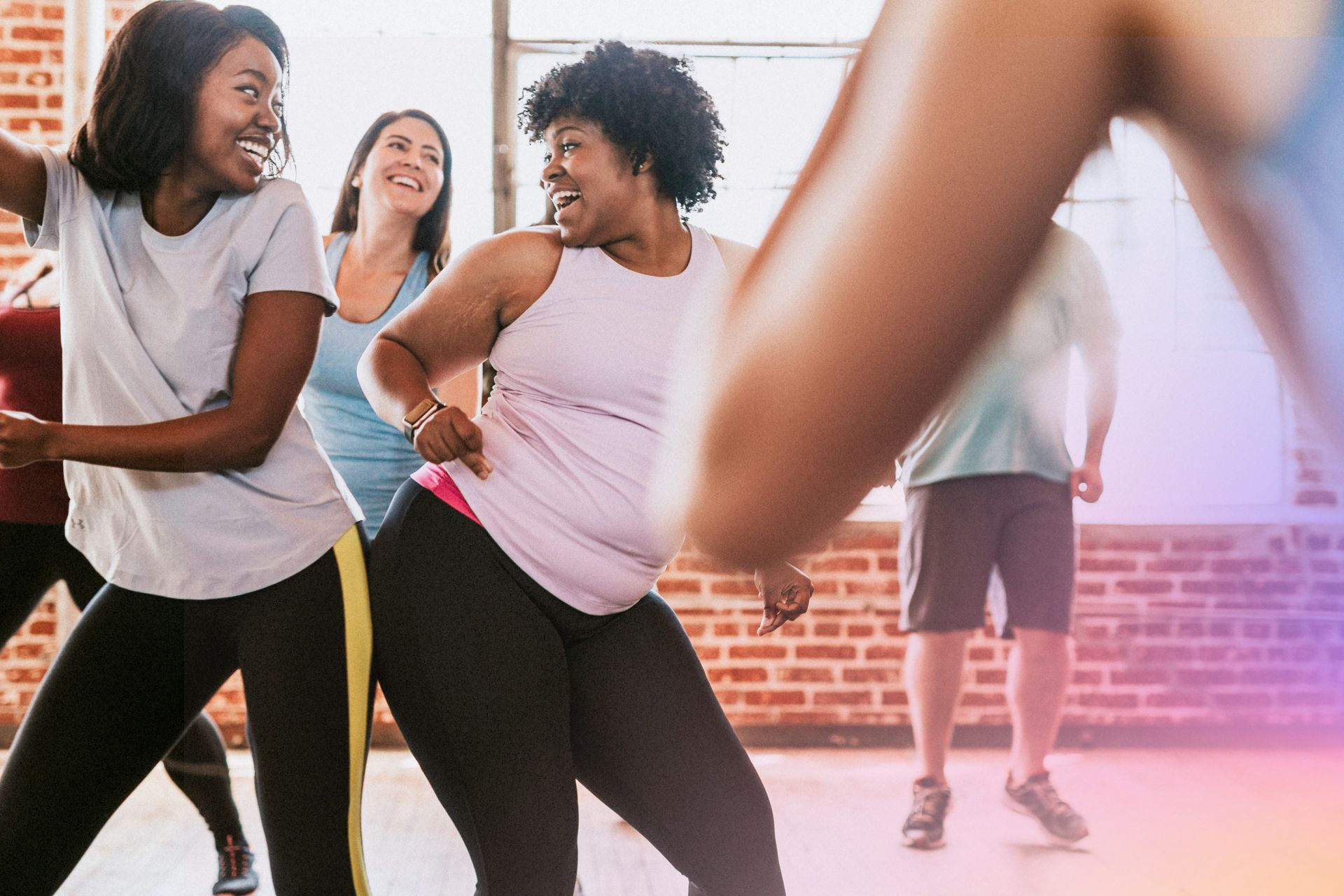Des gens en tenue de sport dansant et souriant dans un studio.