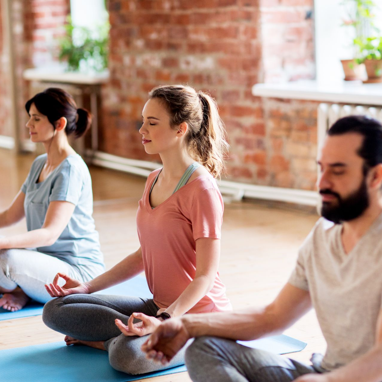 Des personnes méditant dans un cours de yoga, assises sur des tapis, les yeux fermés, dans un studio.