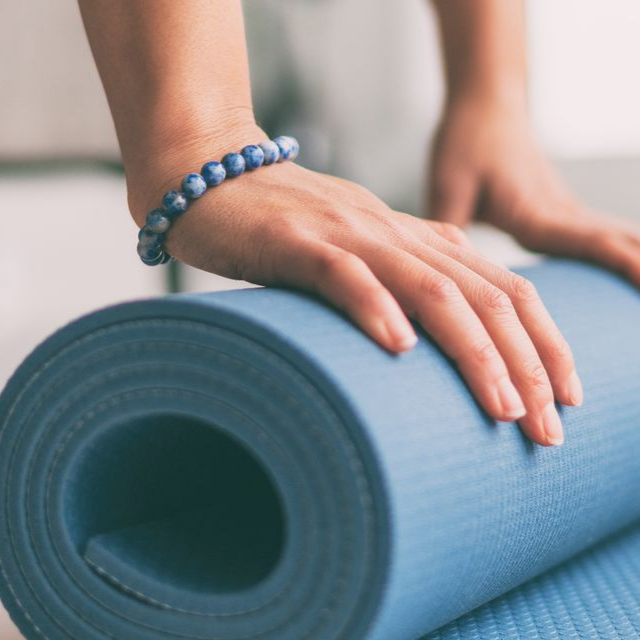 Personne enroulant un tapis de yoga bleu, mains en vue, bracelet bleu.
