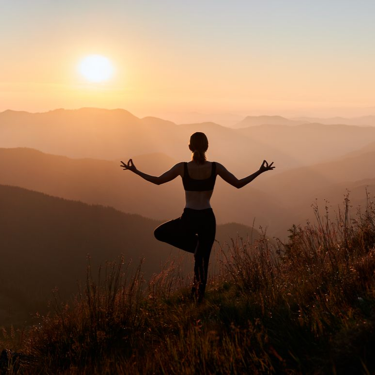 Femme en posture de yoga au sommet d'une montagne au coucher du soleil.