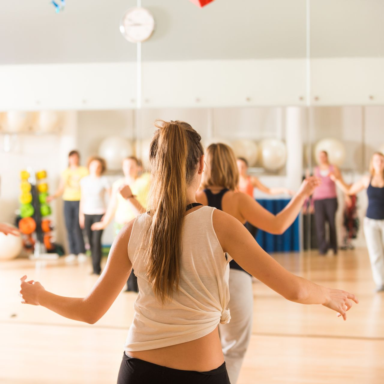 Des gens dansent dans un studio, dos tourné, avec un miroir reflétant la pièce et les autres danseurs.