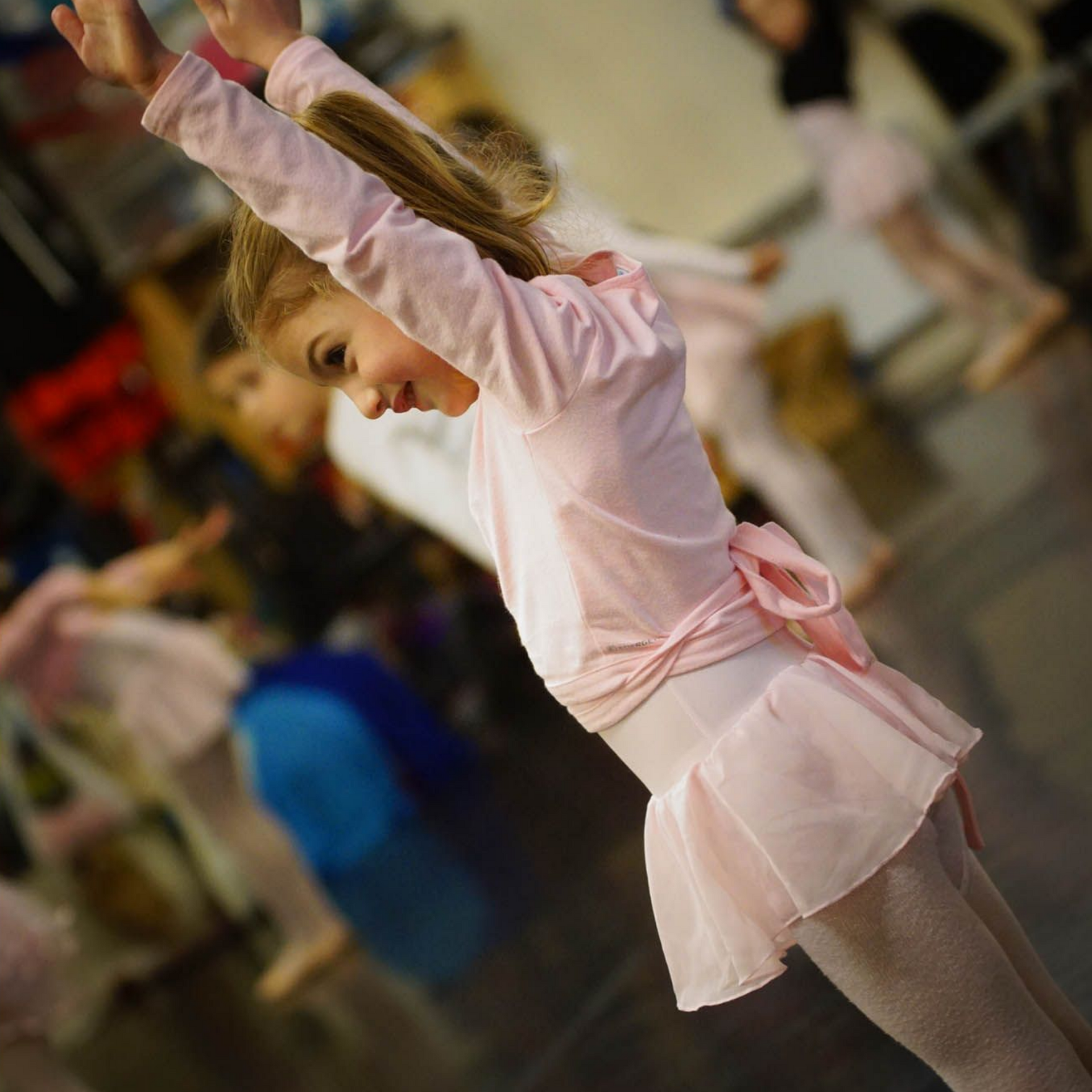 Fille en tenue de ballet rose avec les bras levés pendant le cours de danse.