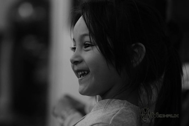 Un enfant avec une queue-de-cheval sourit largement, les yeux fermés, en noir et blanc.