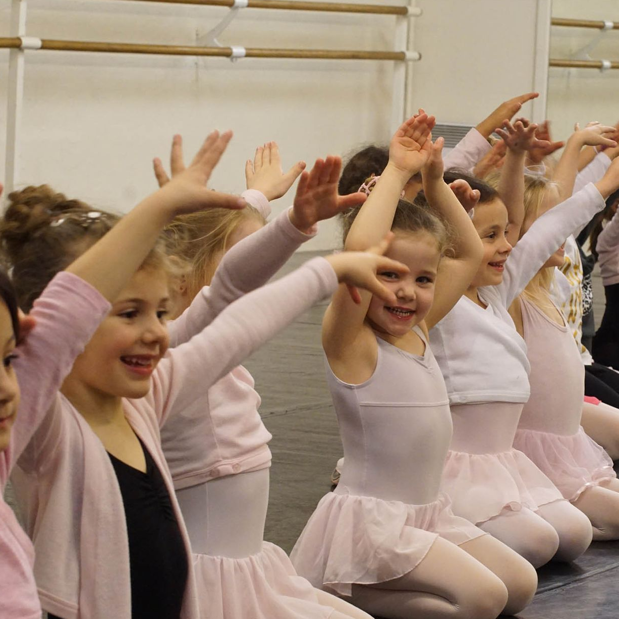 Des enfants en tenue de ballet rose s'étirent dans un studio de danse.