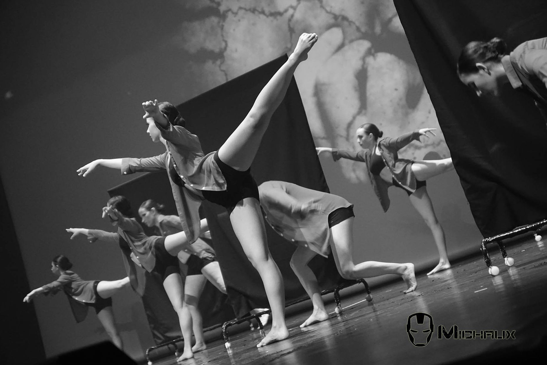 Des danseurs en justaucorps et vestes noirs exécutent une routine de danse moderne sur scène.