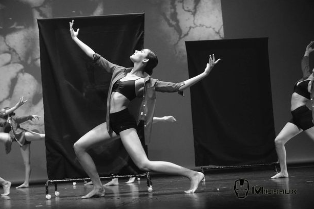 Danseurs sur scène ; l'un d'eux est au centre, les bras levés, en fente profonde. Photo en noir et blanc.