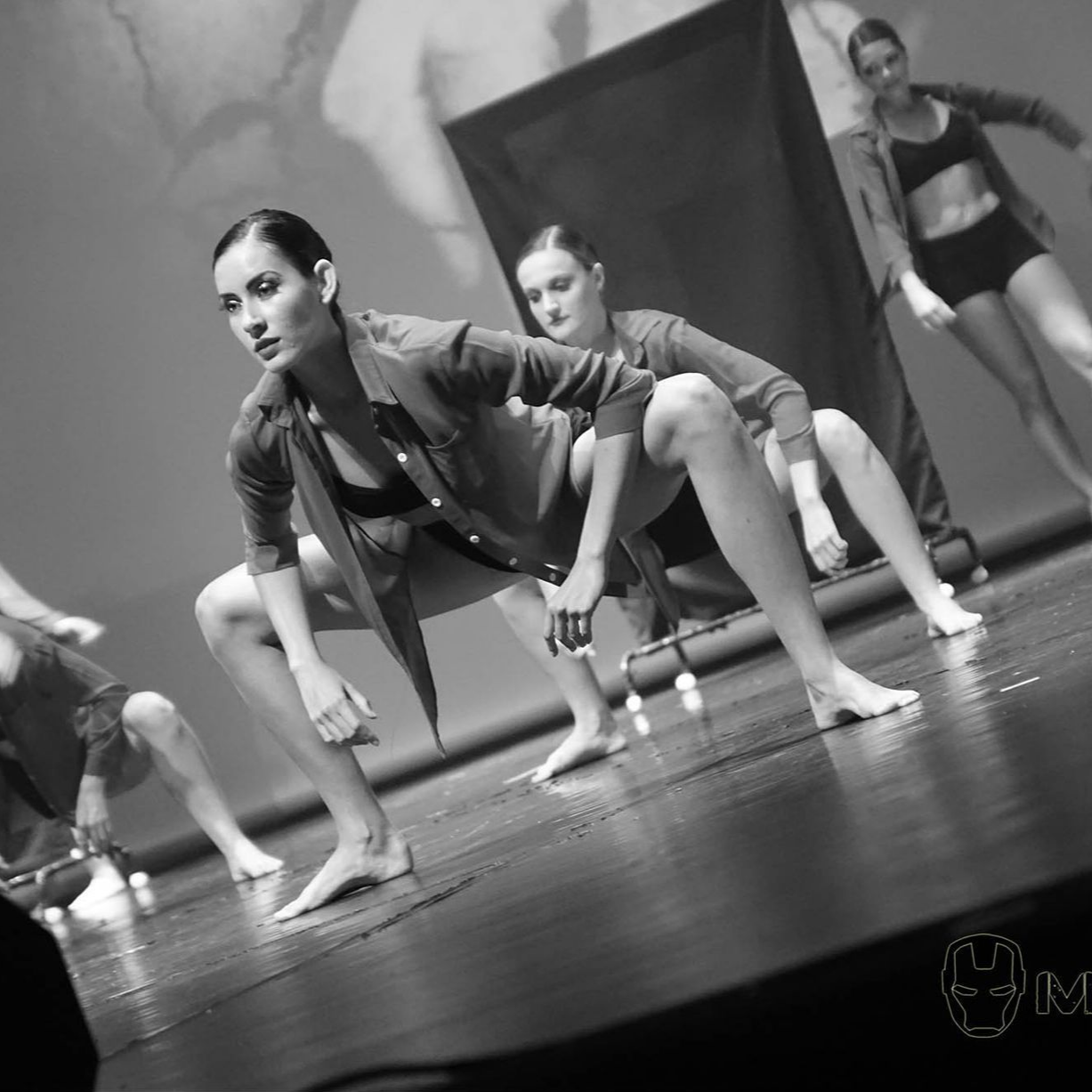 Danseurs dans une performance en noir et blanc. Accroupis, le regard fixé sur un fond sombre.