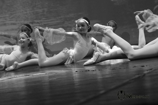 Des danseurs de ballet en justaucorps exécutent un grand écart sur une scène en bois. Noir et blanc.