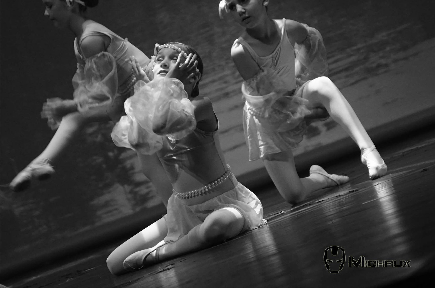 Danseurs de ballet en robes légères sur scène, l'un à genoux et d'autres dans les airs en noir et blanc.