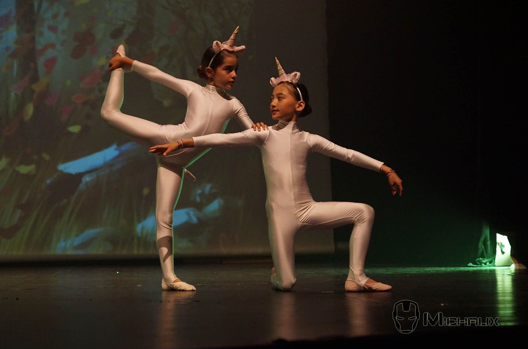 Deux petites filles en costumes de licorne dansent ensemble sur scène.