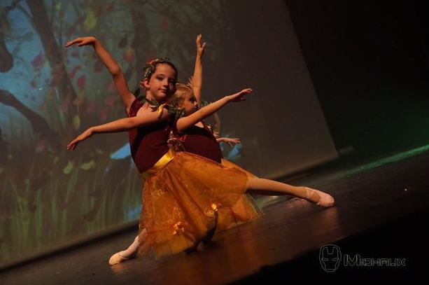 Deux jeunes danseurs en hauts marron et tutus orange exécutant un ballet sur scène.