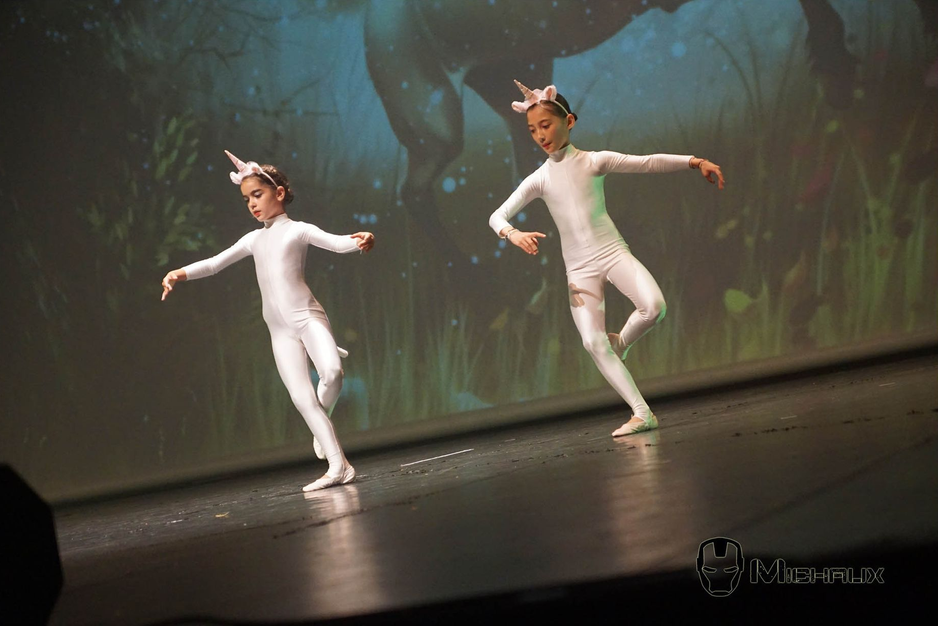 Deux jeunes danseurs en costumes de licorne se produisent sur scène, l'arrière-plan montre une illustration de cheval.