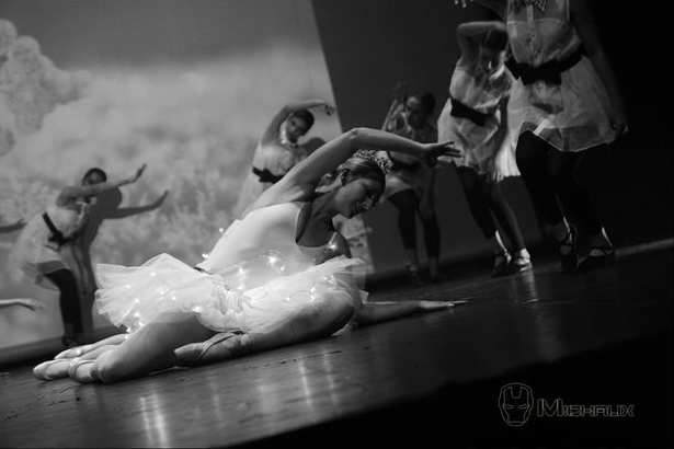 Des danseurs de ballet en tutu blanc se produisent sur scène, un danseur est au sol avec d'autres en arrière-plan.