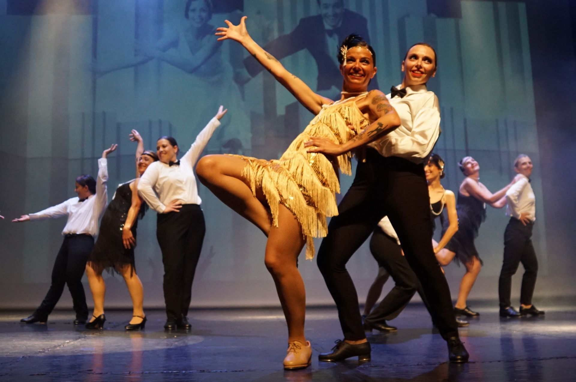 Des danseurs en costumes des années 1920 se produisent sur scène, un couple sous les projecteurs.