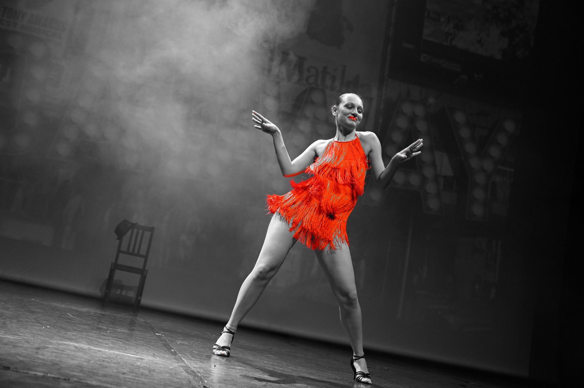 Femme dansant sur scène en robe rouge à franges, fond noir et blanc.