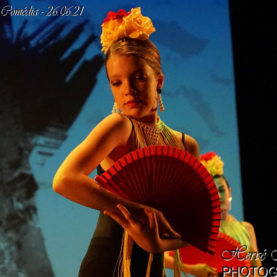 Une fille en robe noire danse le flamenco, tenant un éventail rouge, avec des fleurs dans ses cheveux.