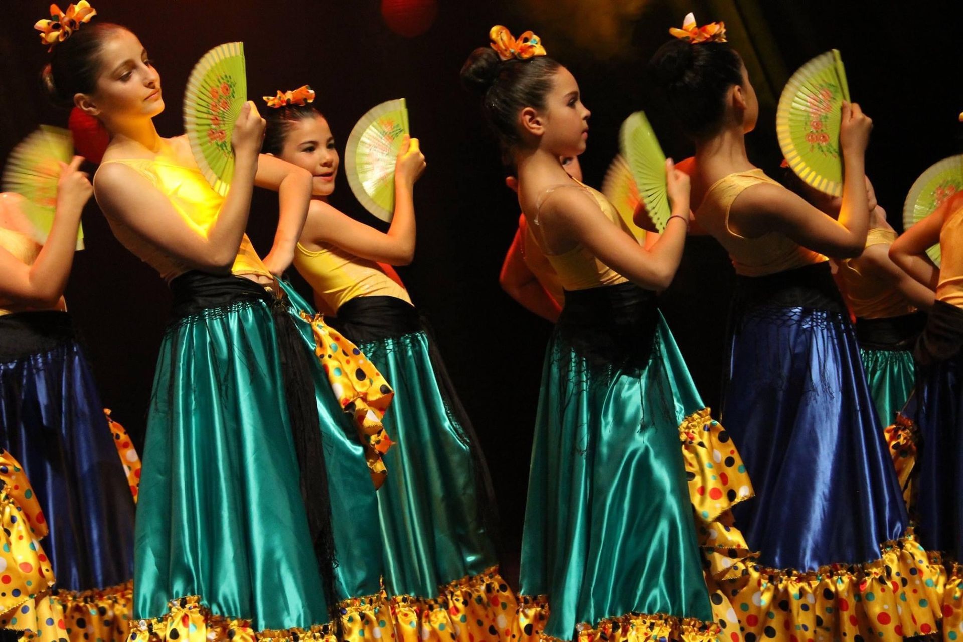 Des danseurs en jupes et hauts colorés, tenant des éventails, se produisent sur scène.