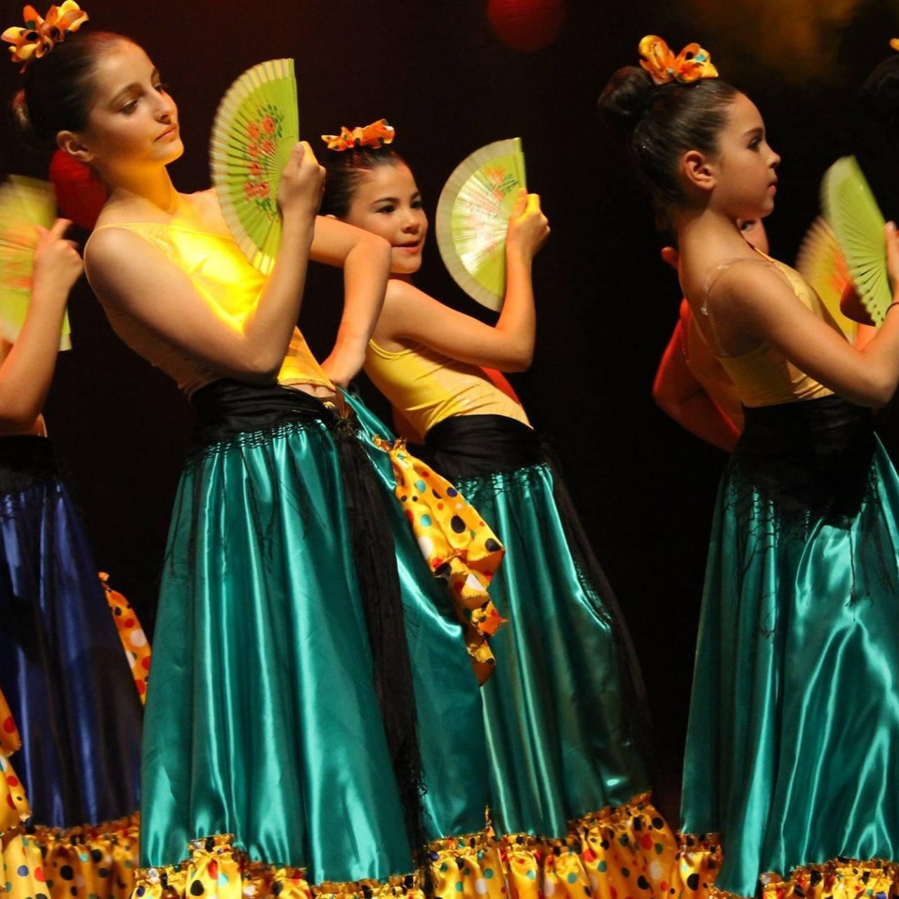 Des danseurs en jupes bleu sarcelle et hauts jaunes se produisent avec des fans sur scène.