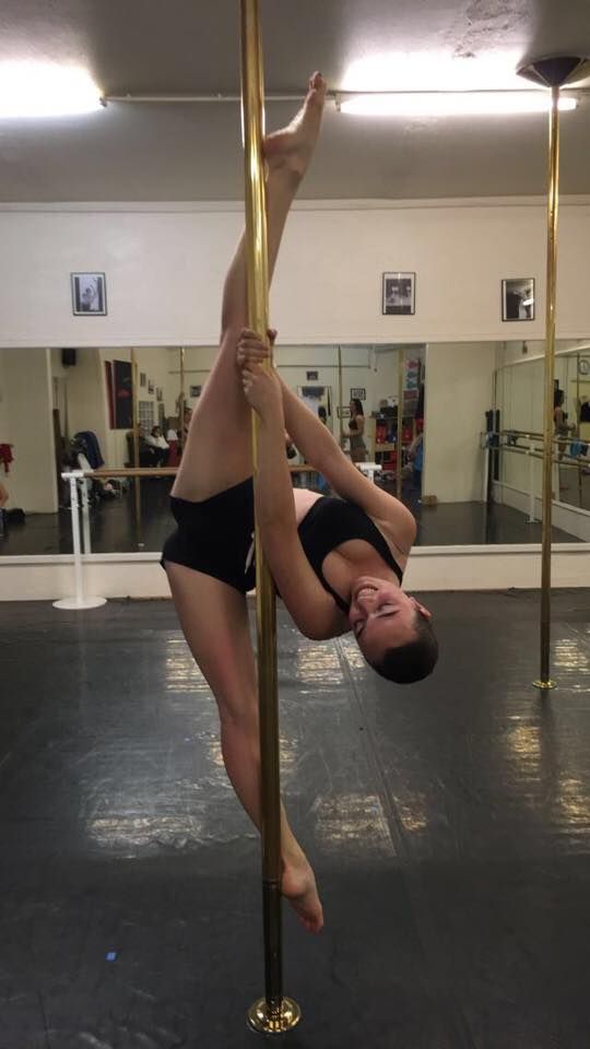 Une femme en tenue de sport noire effectue un grand écart à l'envers. Salle de sport, barre dorée.
