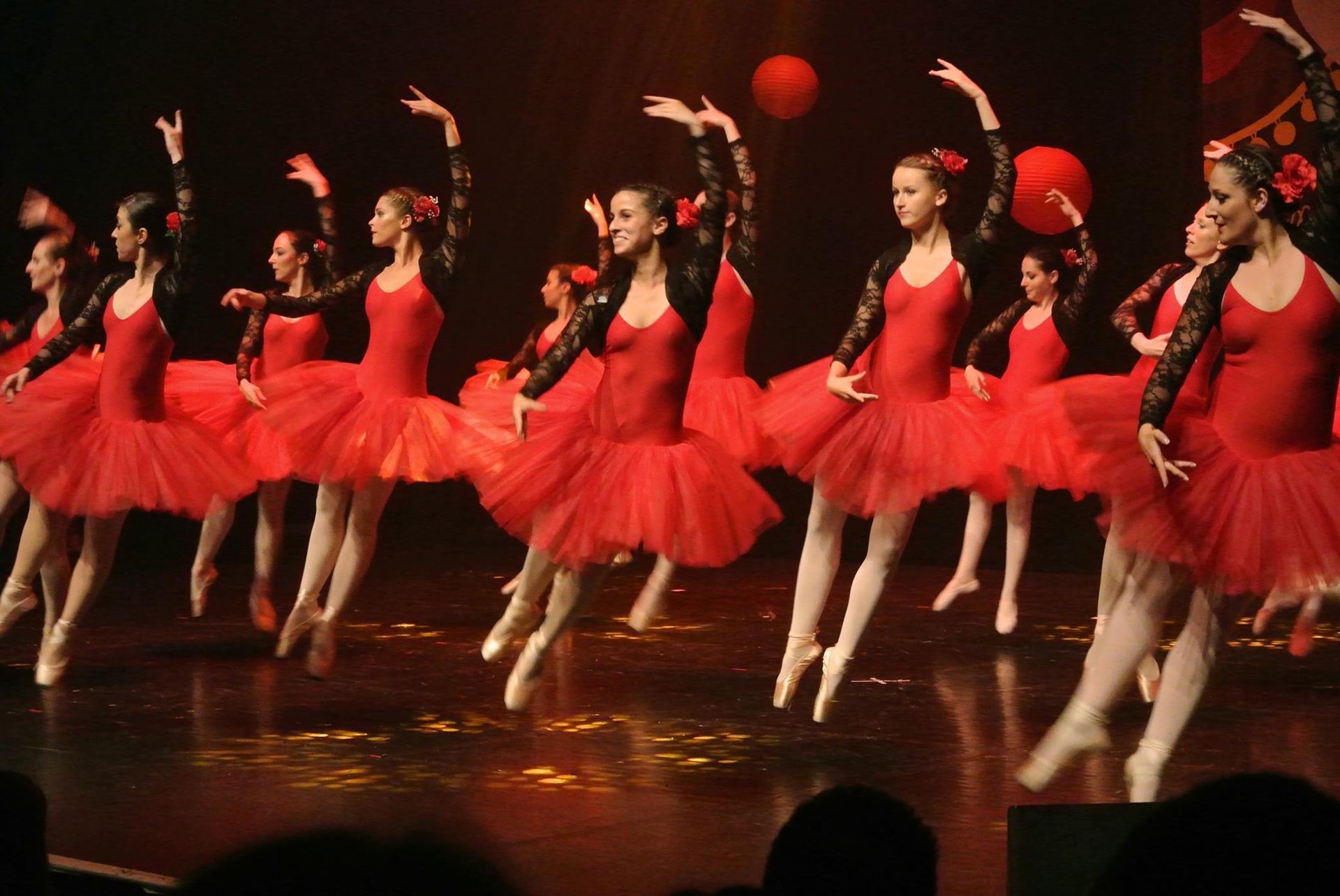 Des danseurs de ballet en tutus rouges sautent sur scène, les bras levés, sous les projecteurs.
