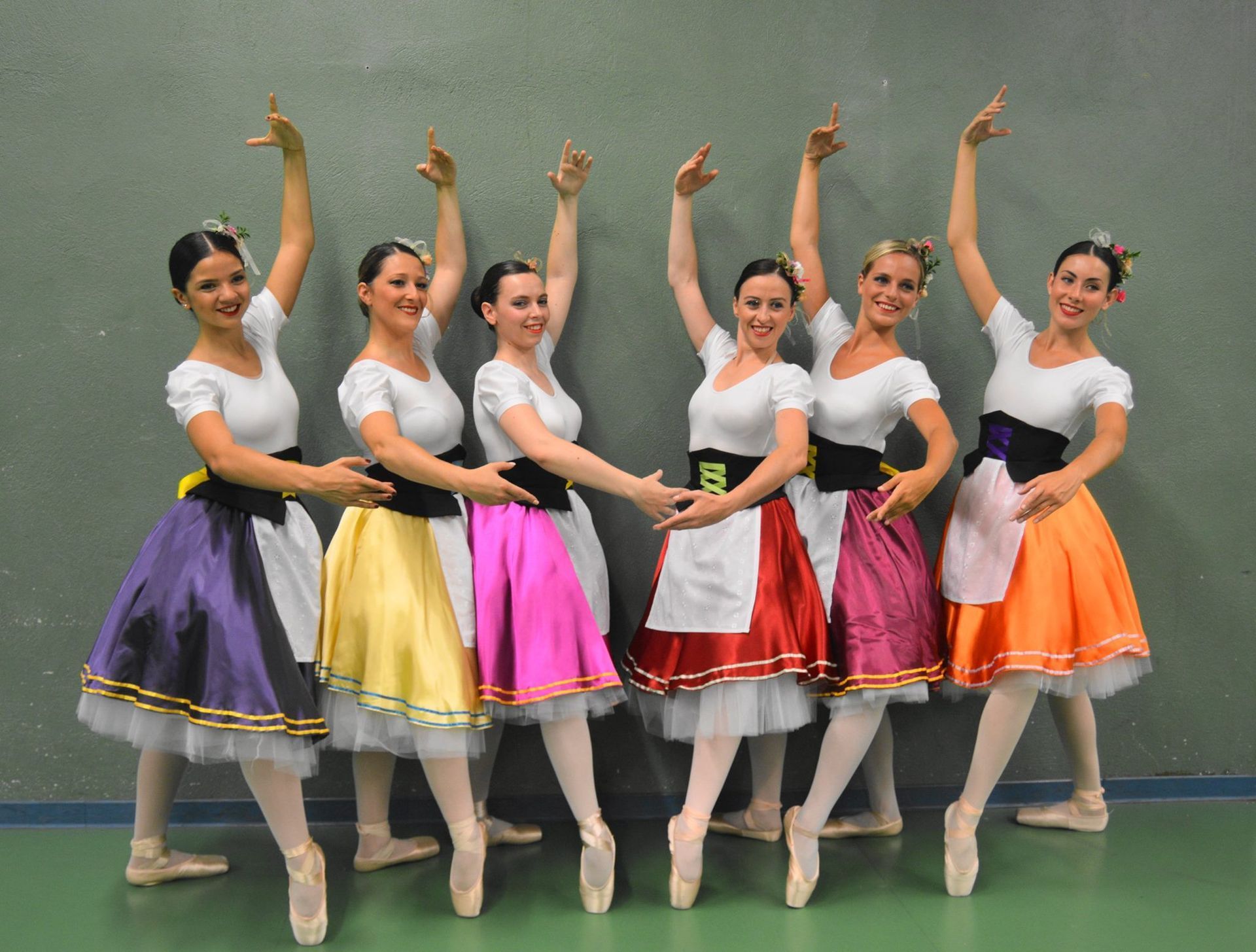 Des danseurs de ballet en jupes colorées posent avec les bras levés et se produisent sur scène.
