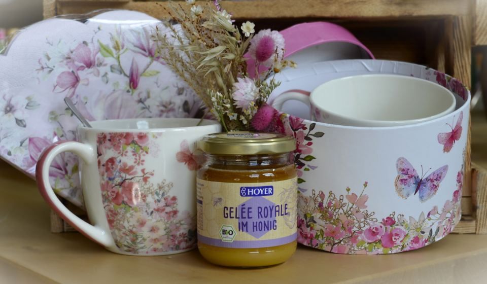 Ein Glas Honig steht neben einer Tasse auf einem Tisch.